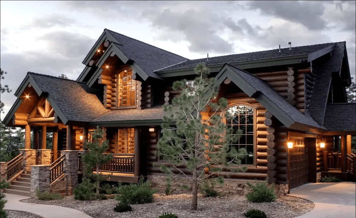 Finished cedar log home exterior at dusk with covered porch and stone accents