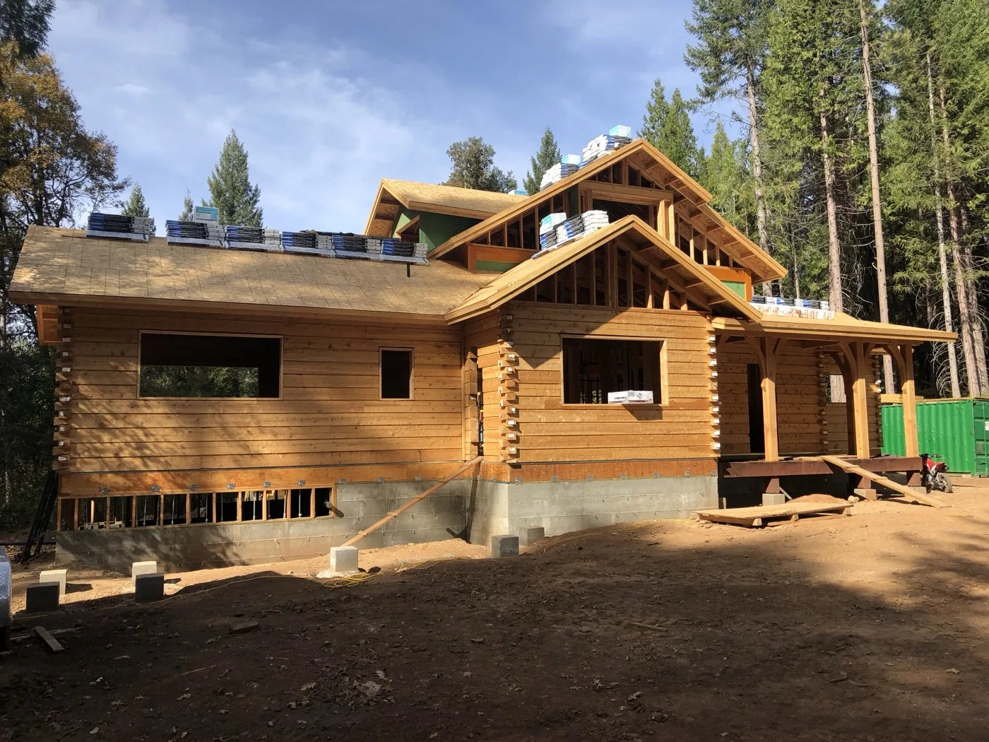 Log home under construction with new roof shingles and covered porch framing in the pines