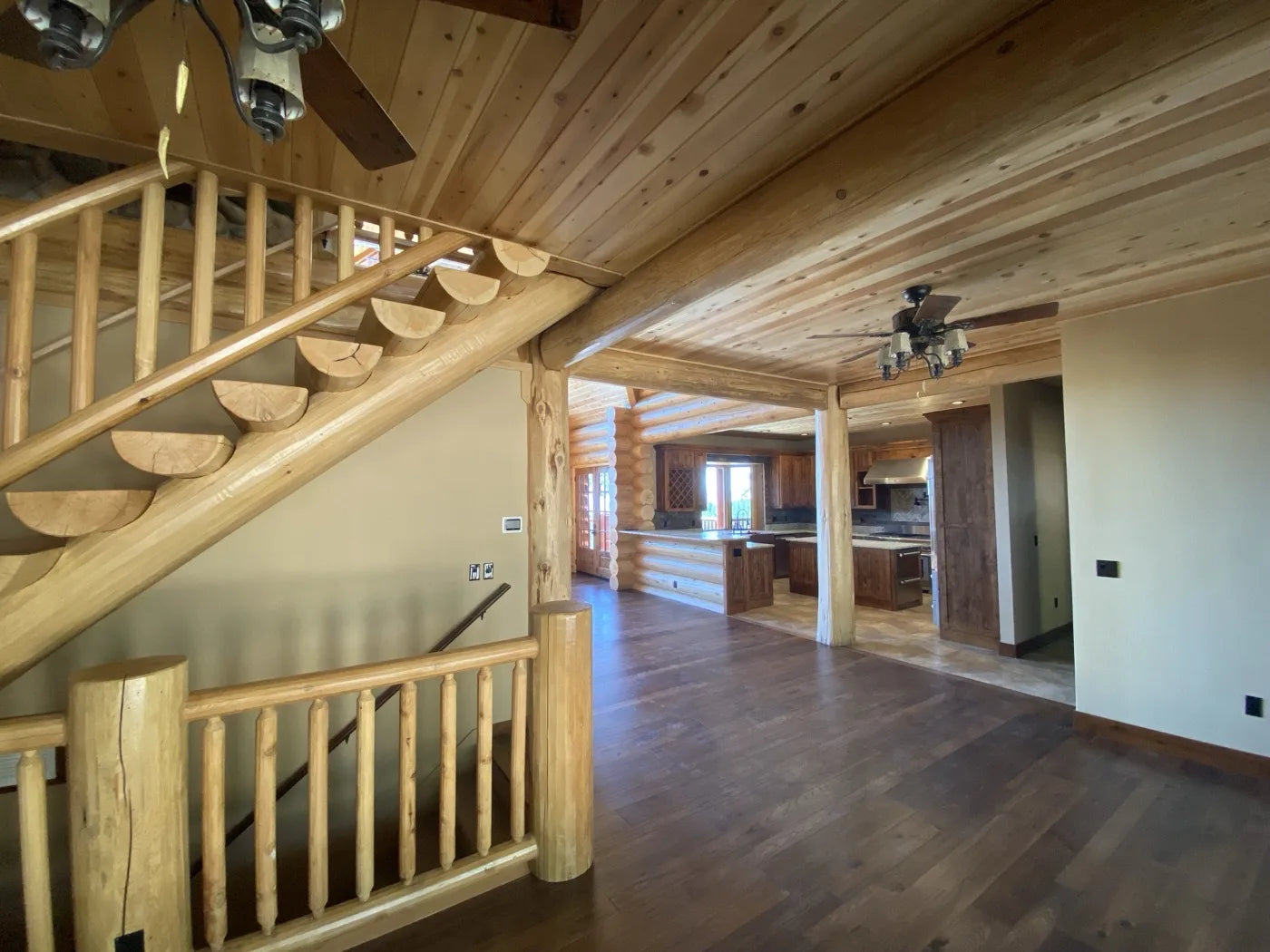Log home great room interior with log staircase and open kitchen under wood ceiling beams