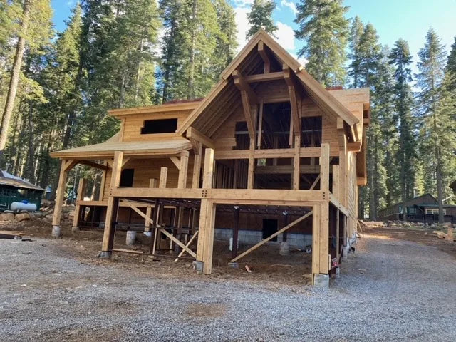 Snow-covered log home at golden-hour sunrise with equipment in the yard