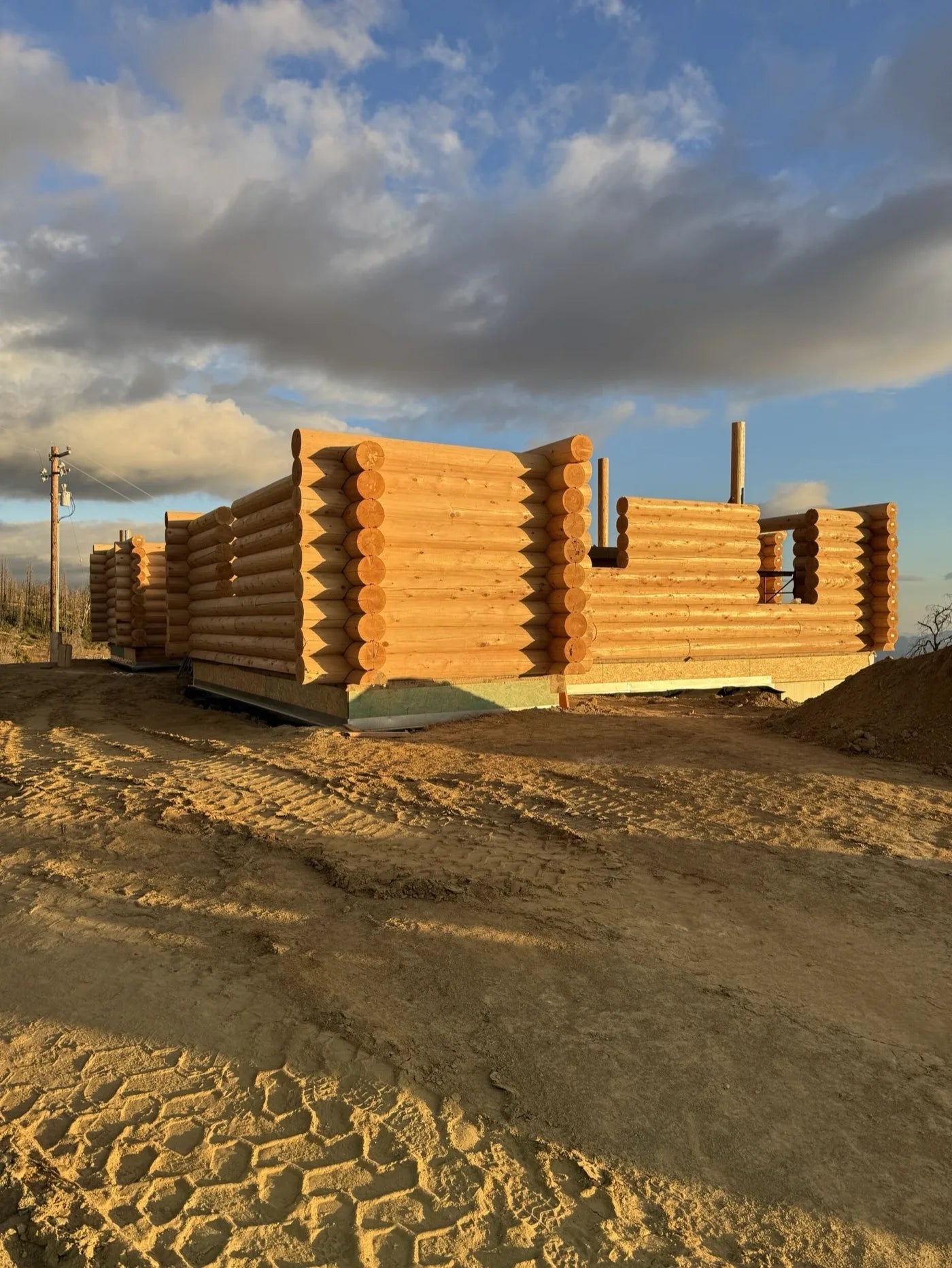 Aerial view of stacked log home walls glowing gold at sunset above the ridgeline