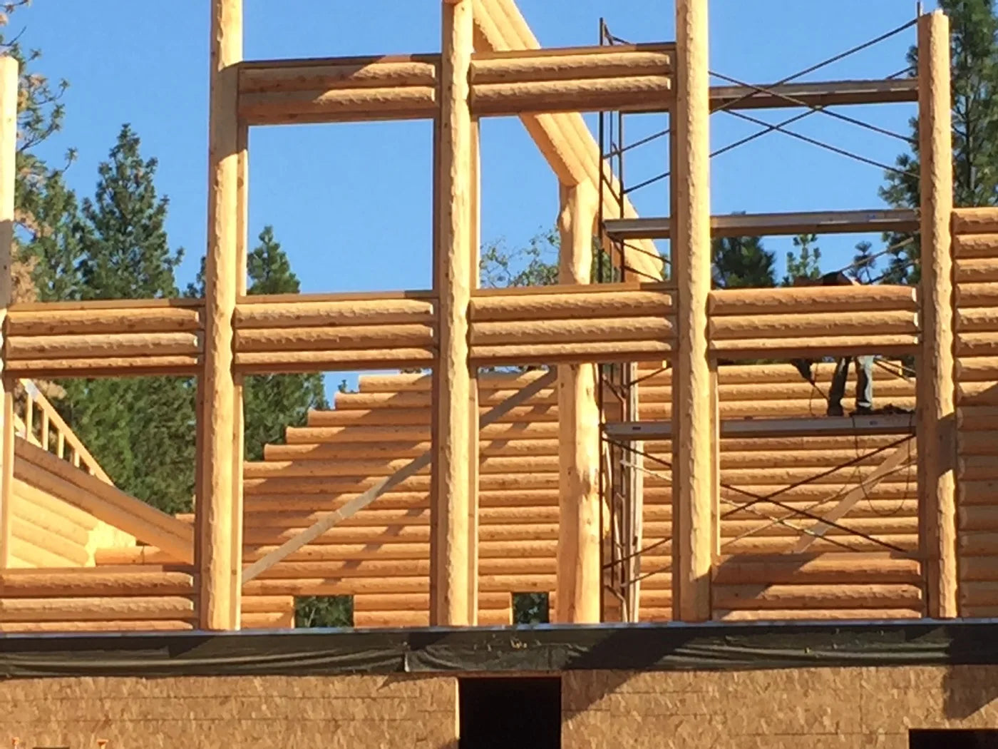 Exposed roof framing and log wall corner with workers on scaffolding