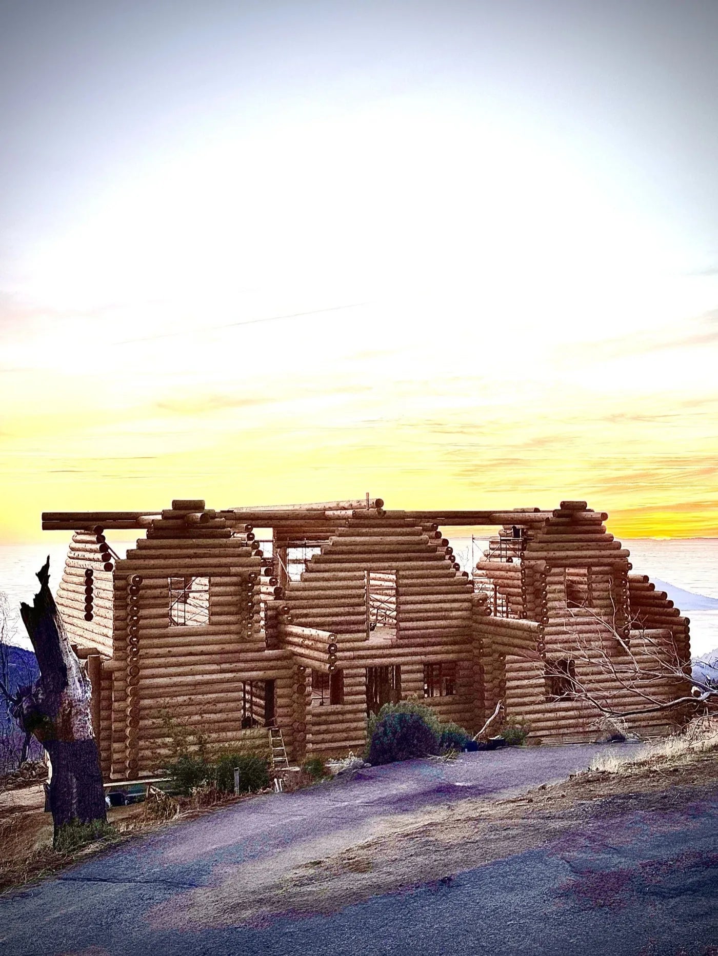 Two-story log home shell nearly framed against a dramatic sunset sky