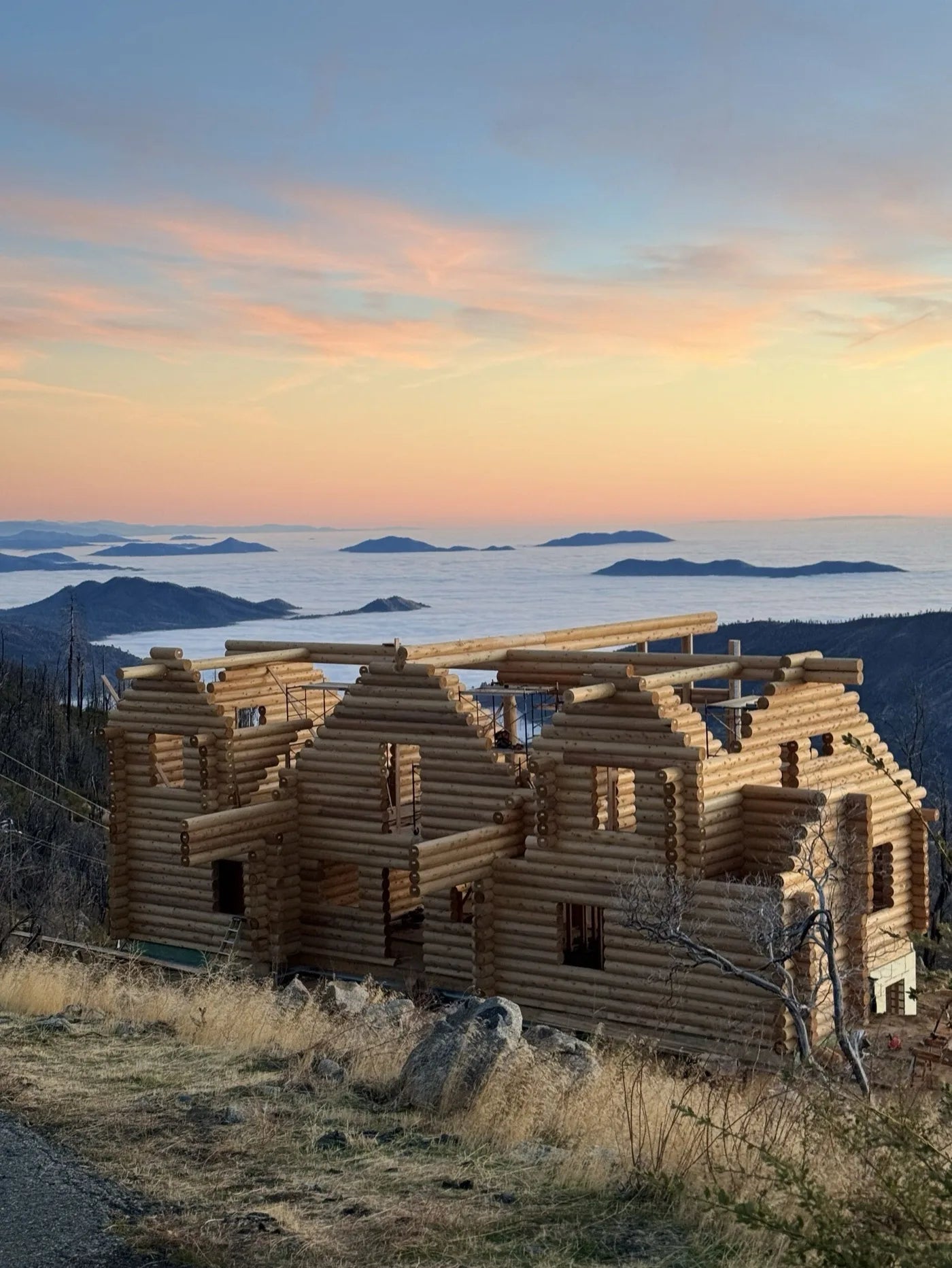 Log home shell under construction overlooking a cloud-covered valley at sunset