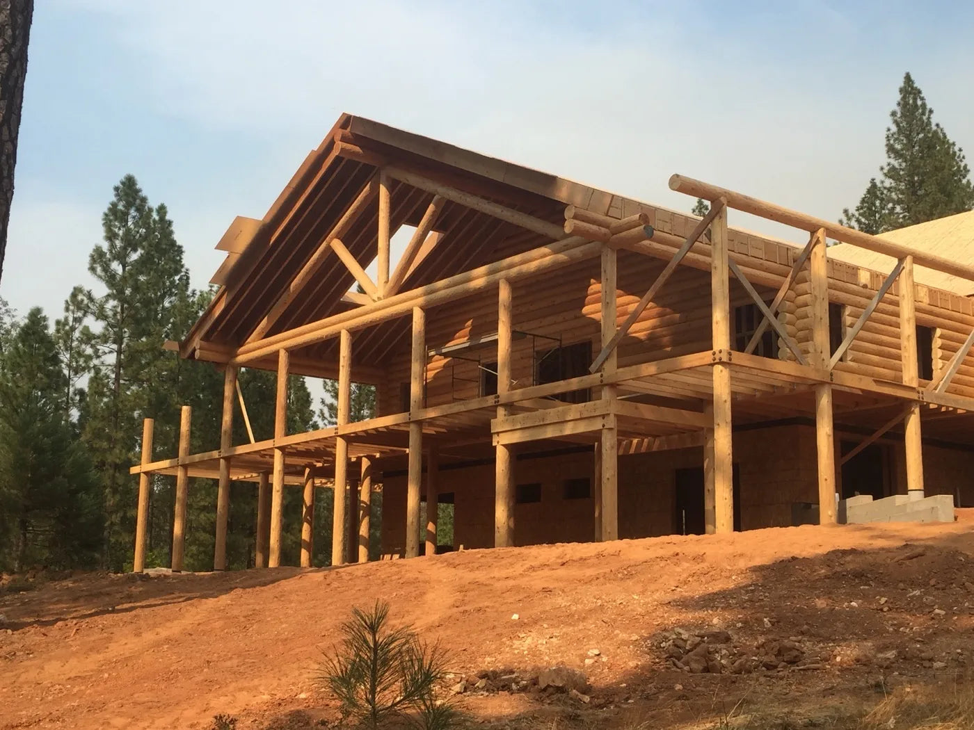 Log home covered deck framing with support posts in a forested lot