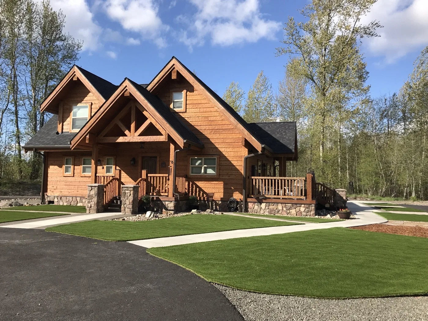 Finished single-story log home with covered porch and manicured lawn on a sunny day