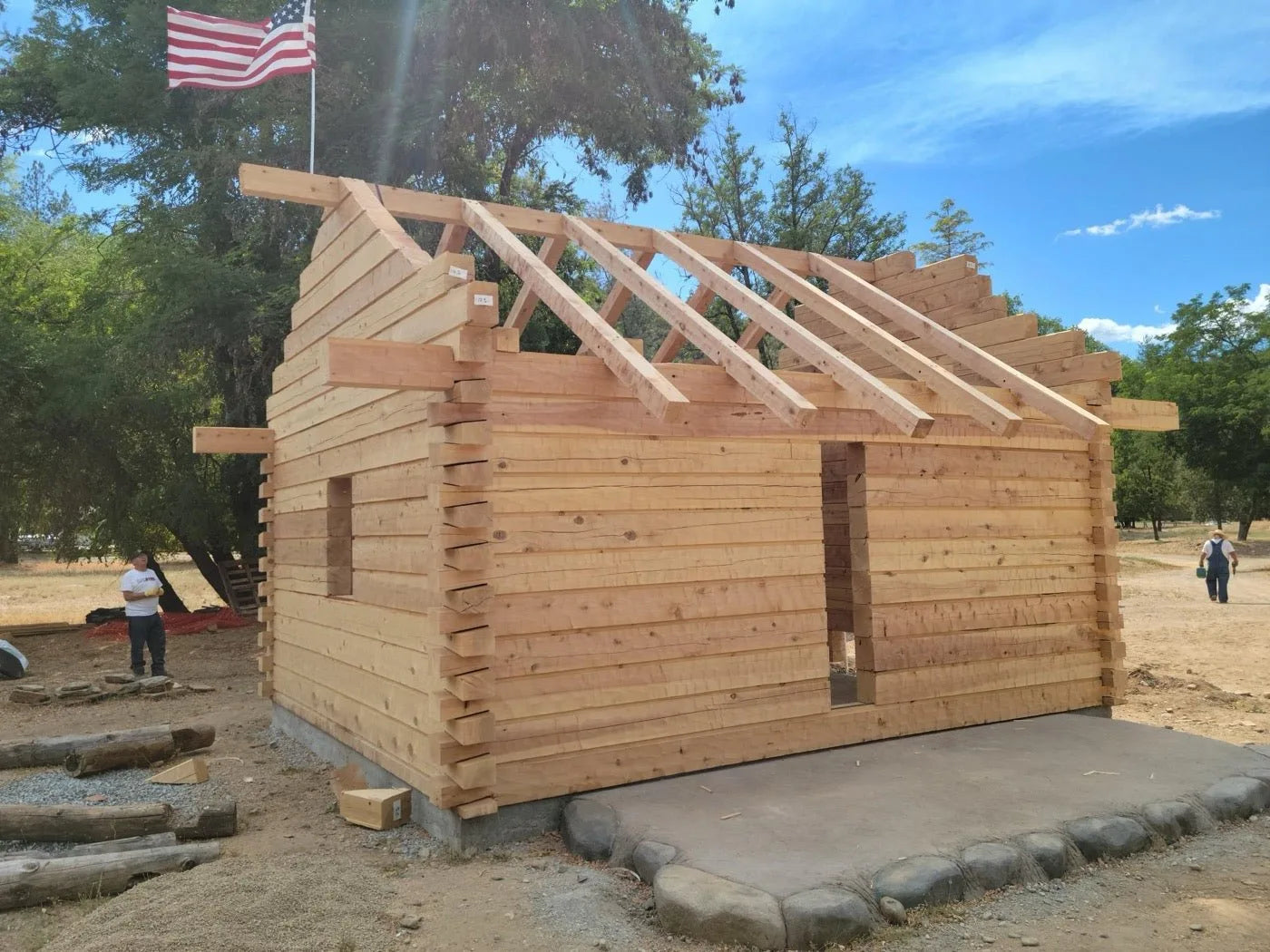 Log cabin walls and roof trusses framed with an American flag flying overhead