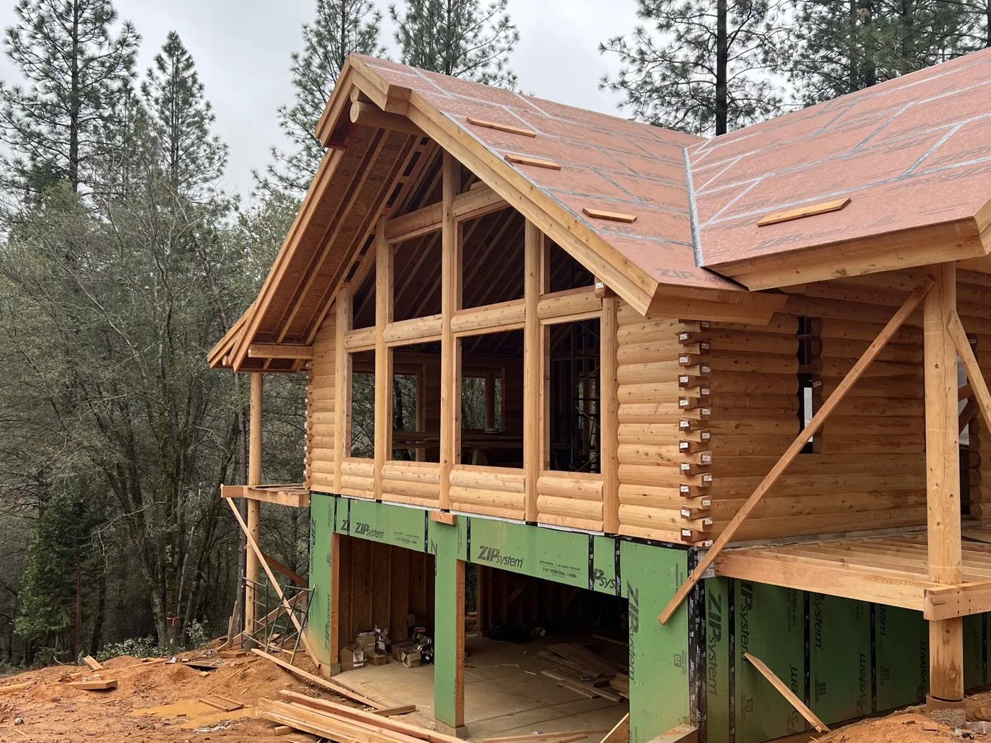 Log home exterior with large window wall and cedar siding nearing completion