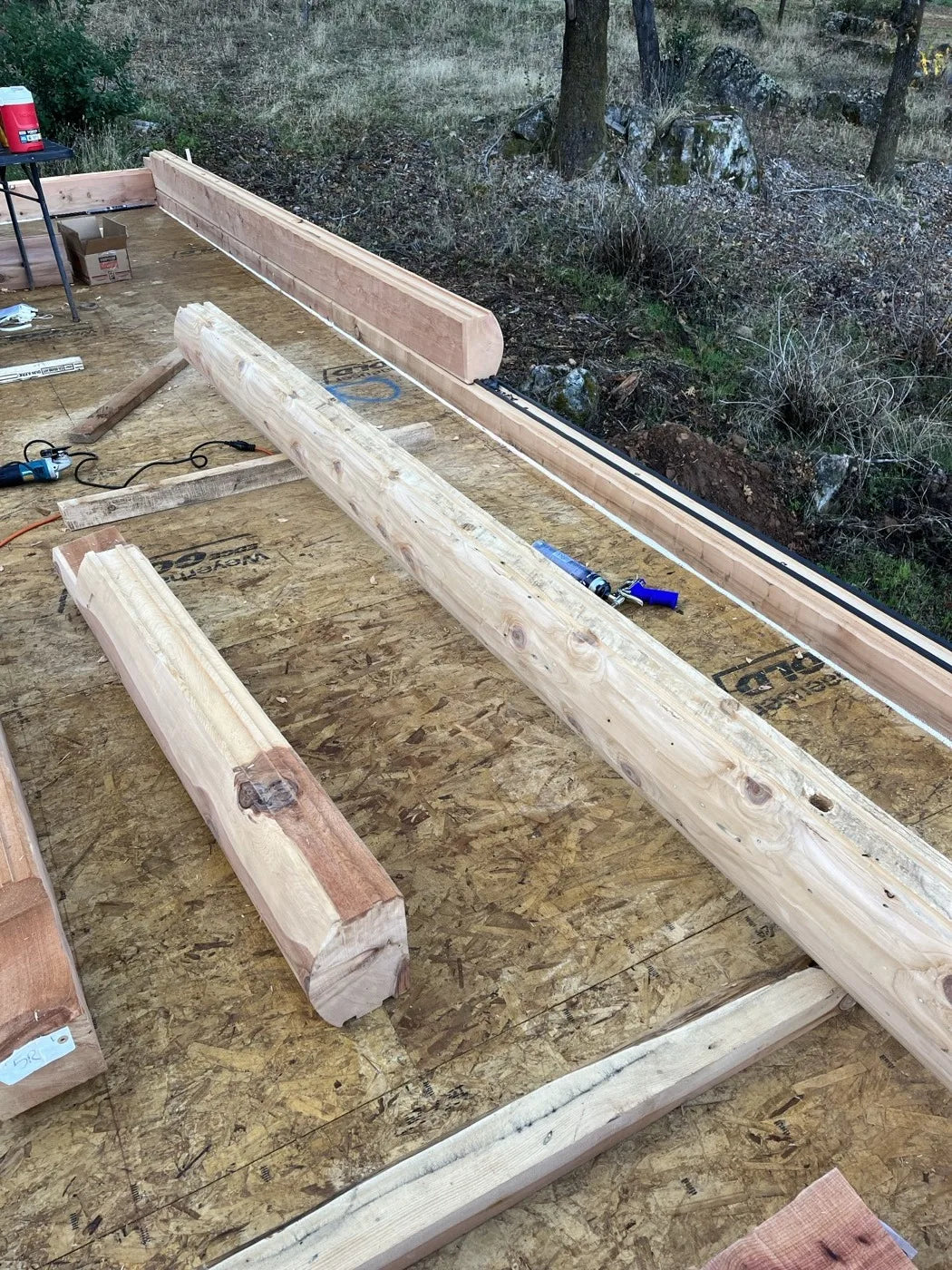 Aerial view of cedar beams and framing lumber staged on the subfloor near the foundation edge
