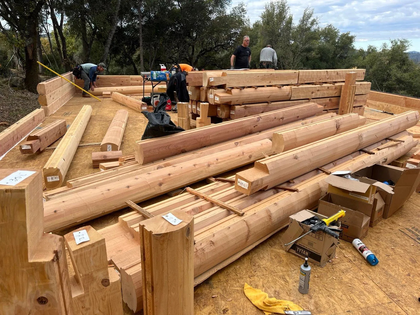 Cedar logs, corner posts, and trim stacked on the framed subfloor