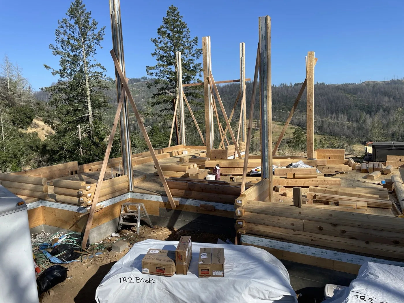Cedar log home under construction with large window wall and covered entry