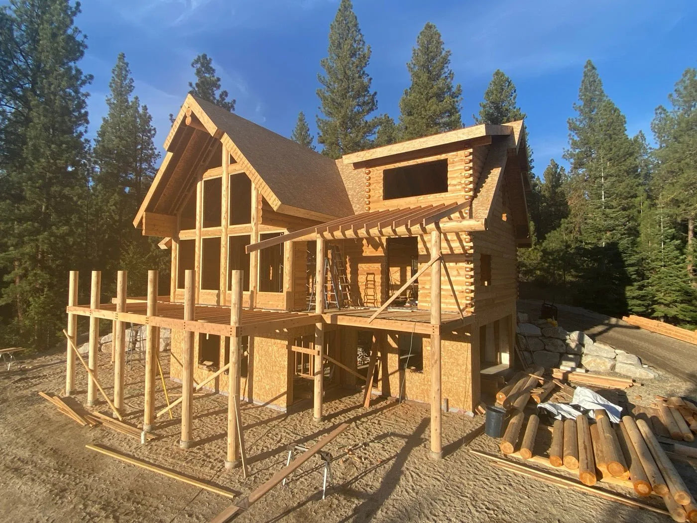 Two-story log home exterior with covered deck and mountain view at sunset