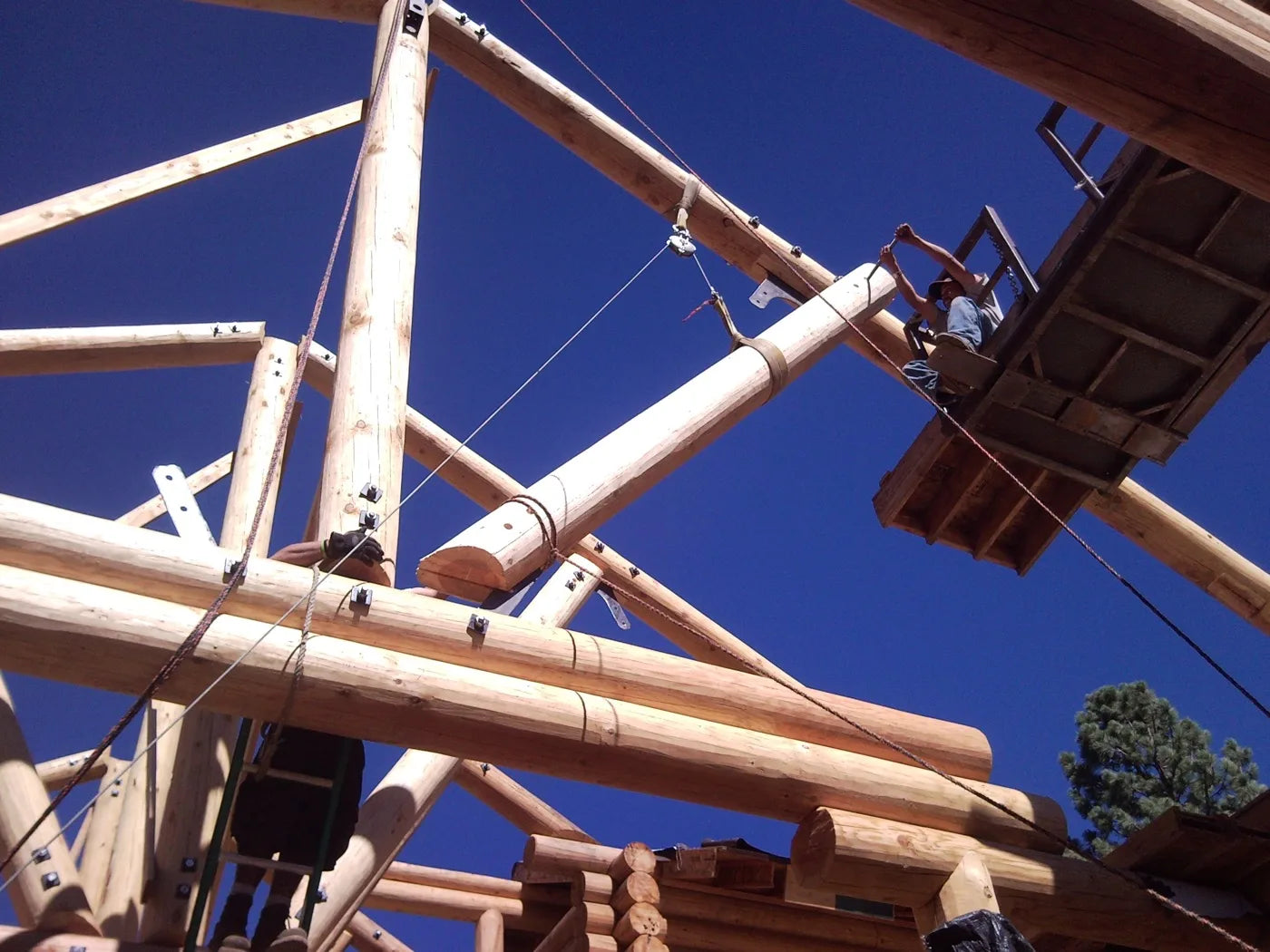 Workers assembling log roof trusses with a crane and lift platform