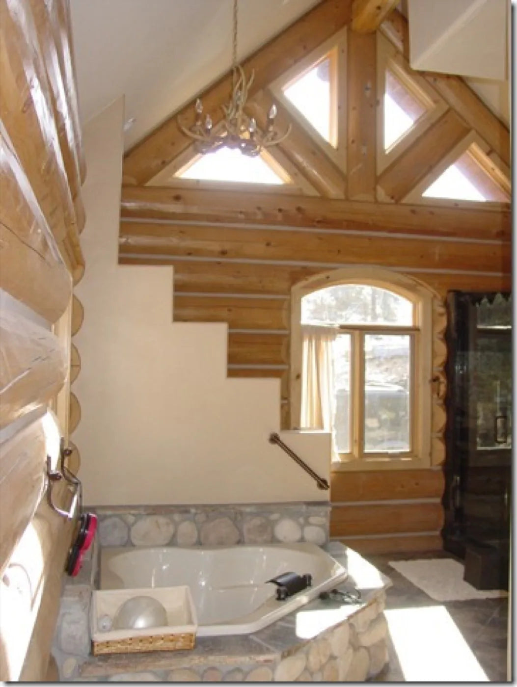 Primary bathroom with a corner soaking tub, river-rock surround, and vaulted log ceiling