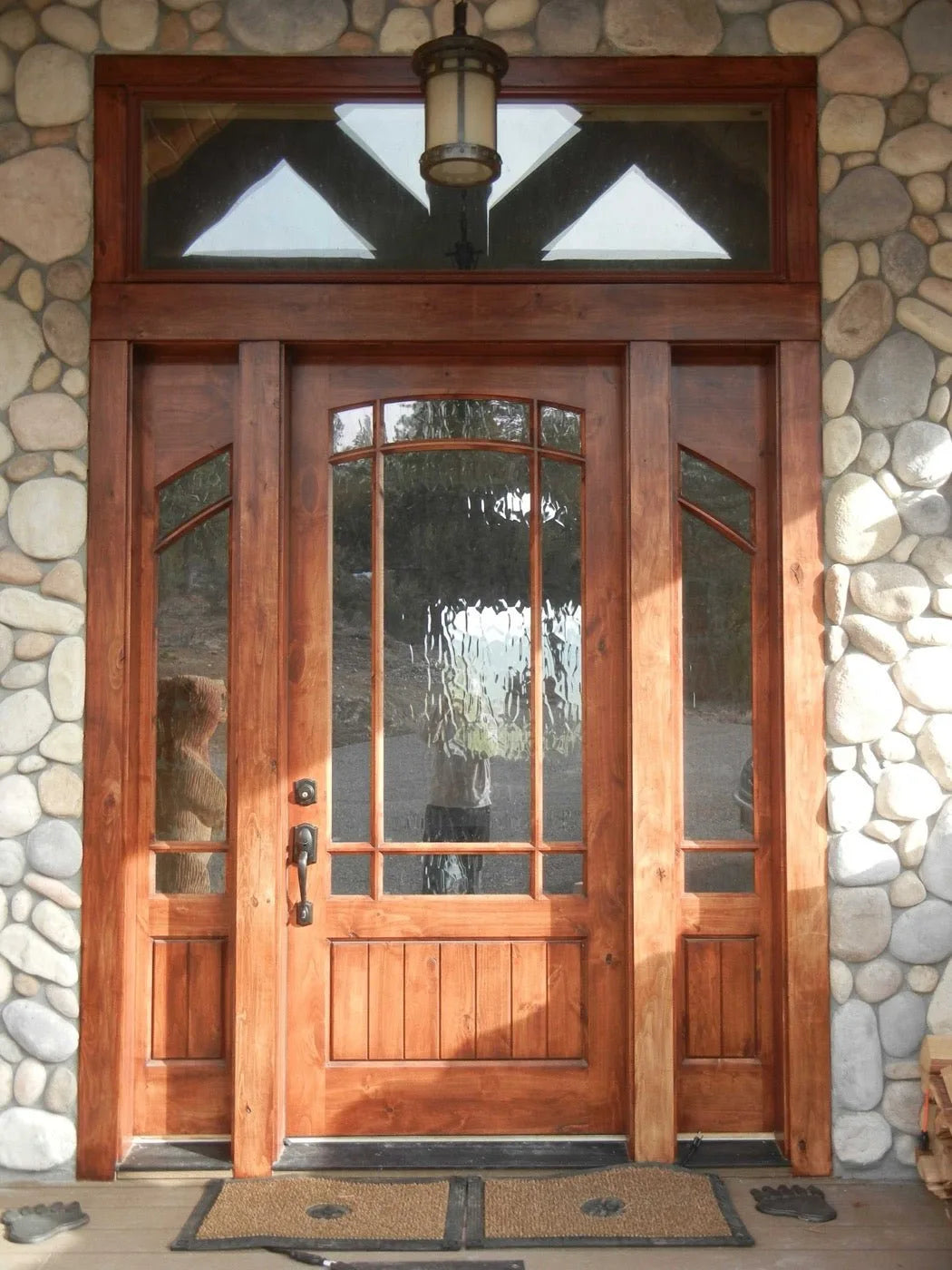 Craftsman-style front entry door with glass sidelights and a river-rock stone surround