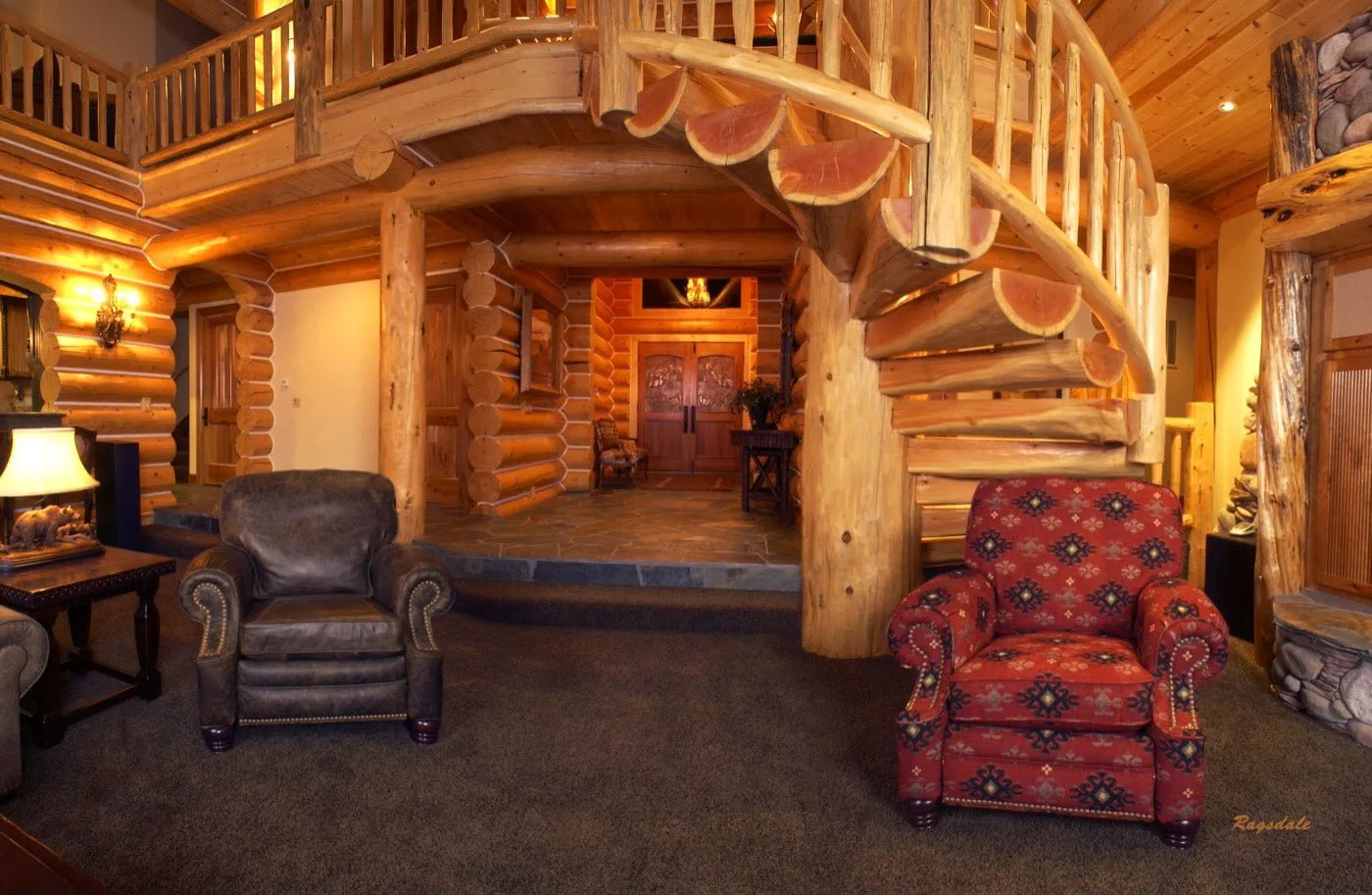 Two-story great room with a curved log staircase leading to a loft and carved double entry doors