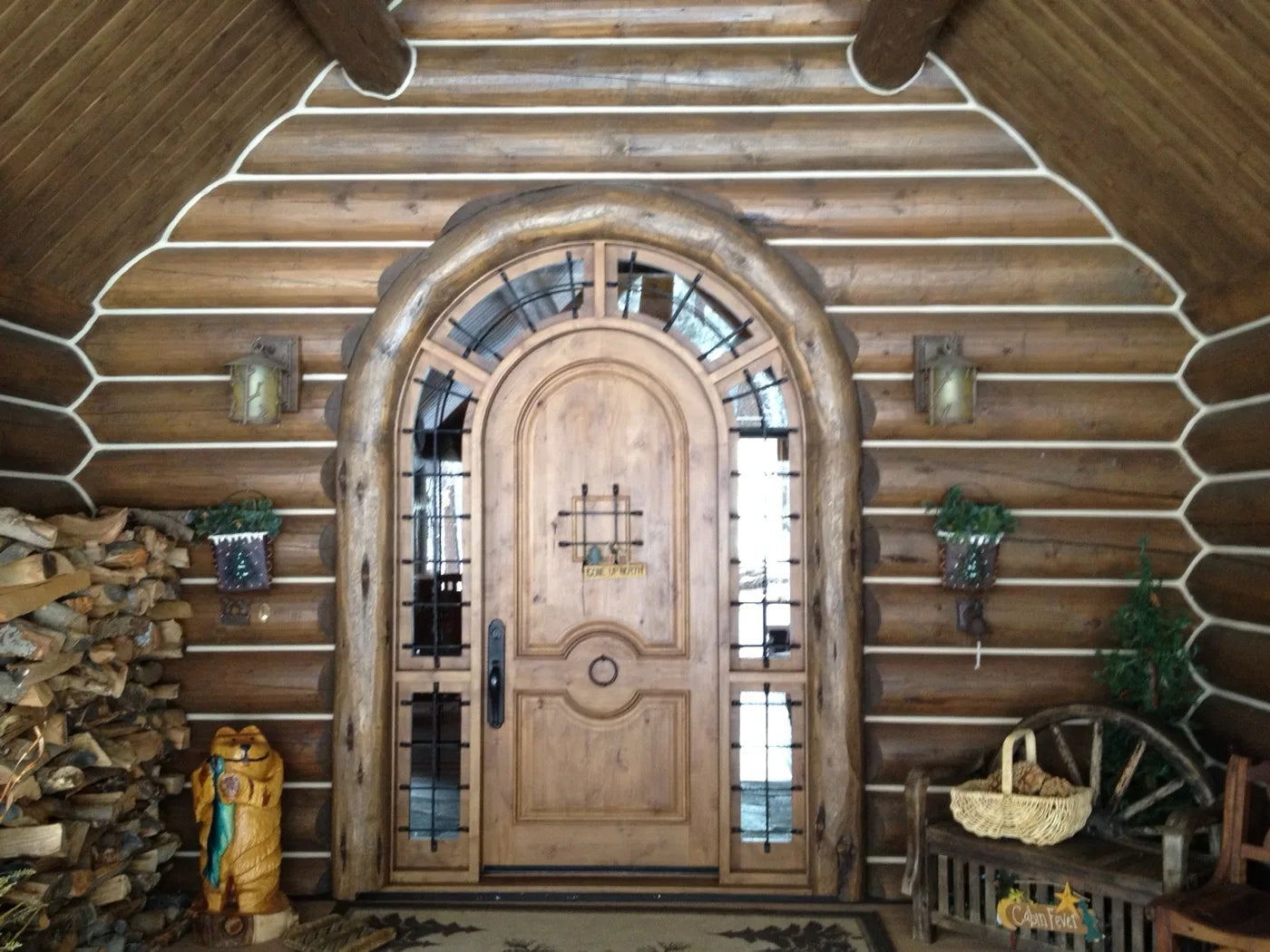 Grand arched log home entry door with iron-strapped glass sidelights and a firewood display