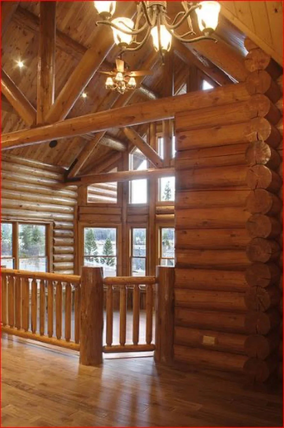 Loft landing with a log railing overlooking tall windows and a snowy mountain view