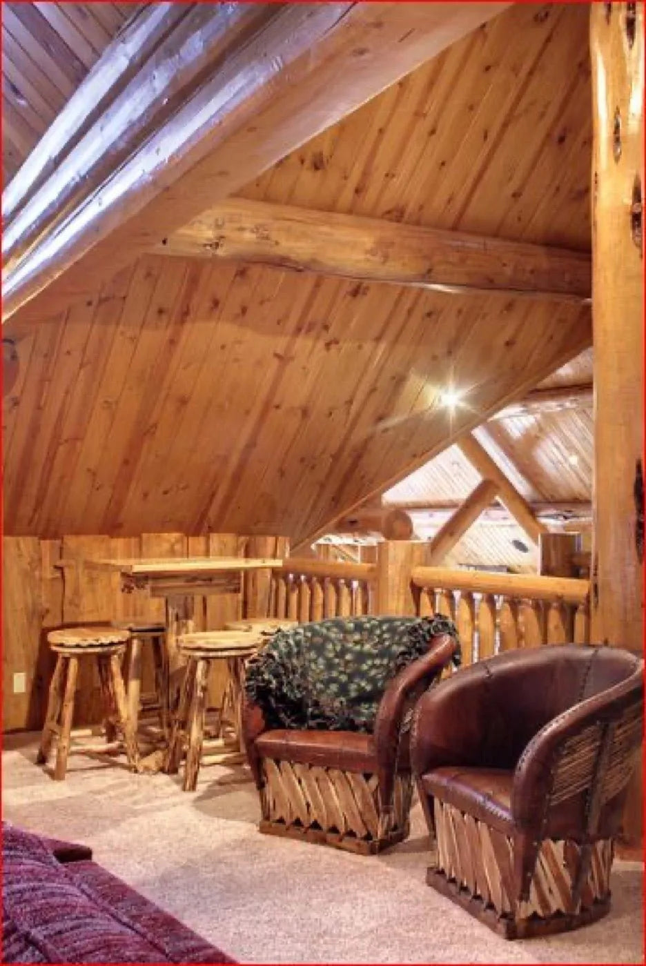 Log home loft with leather barrel chairs and a bar table under a metal roof