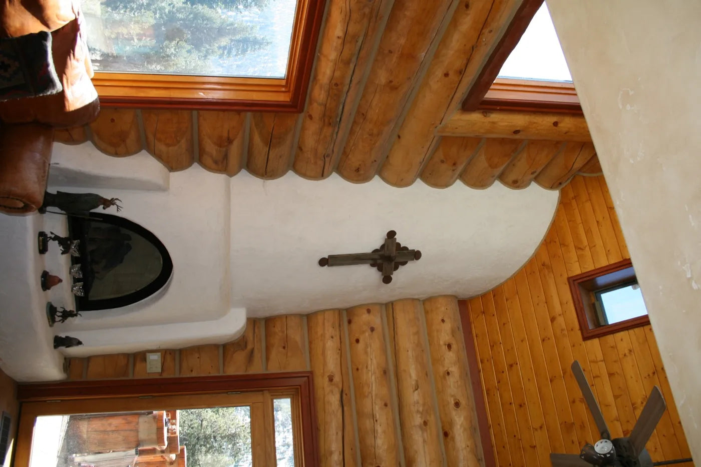 Southwestern-style kiva fireplace with a plastered surround and iron cross in a log home