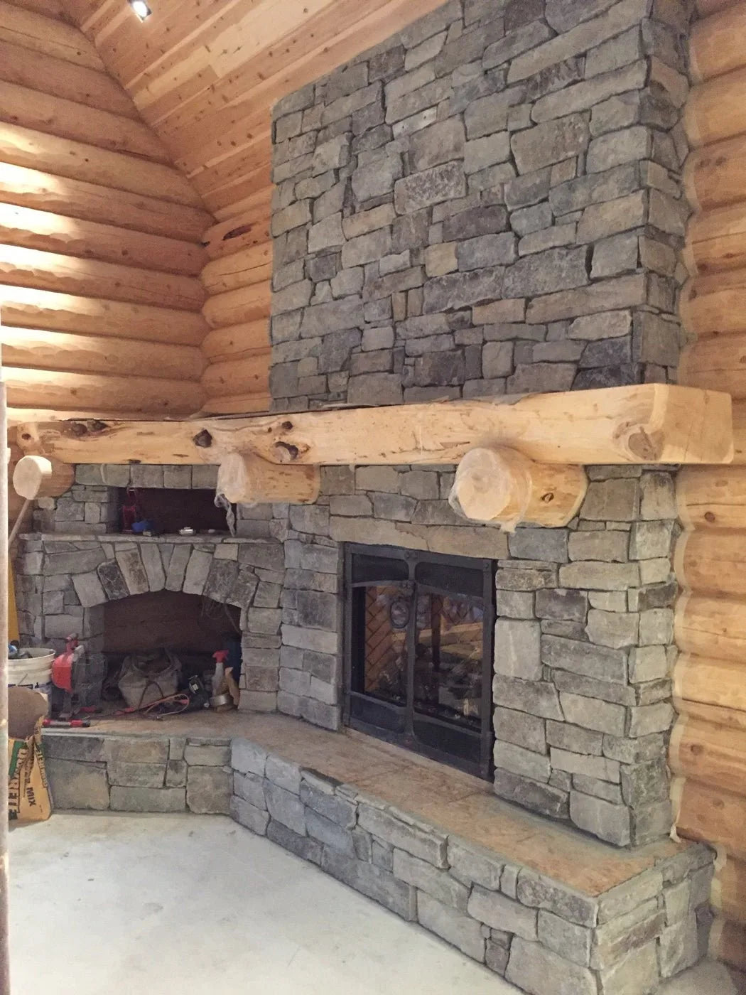Rough stone fireplace under construction with a fresh cedar log mantel
