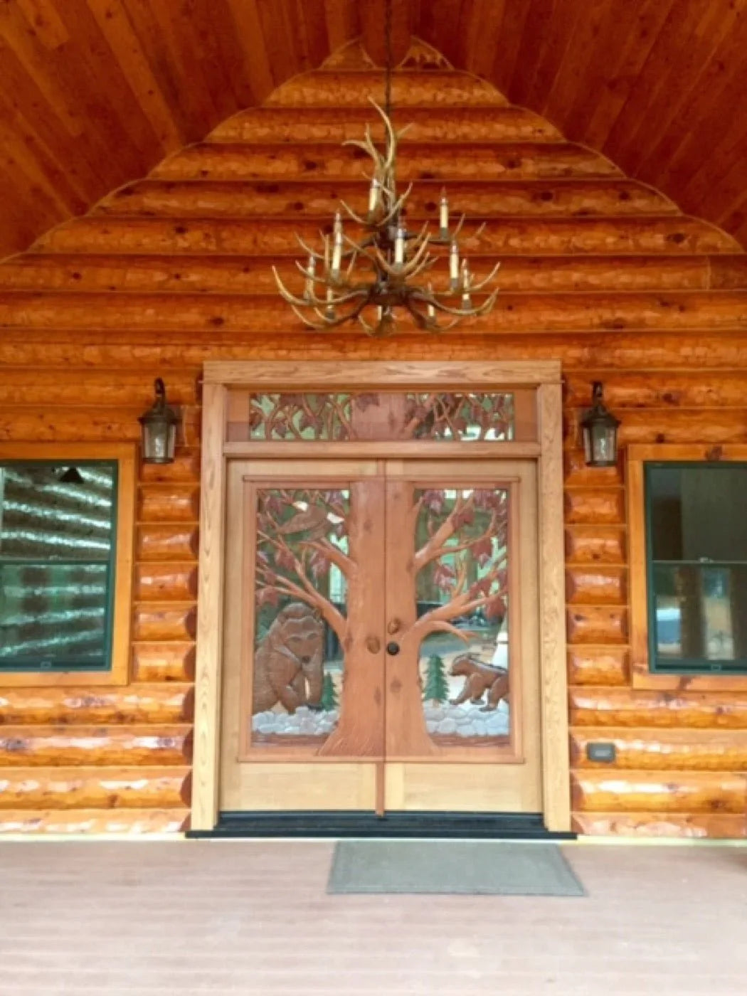 Hand-carved double entry doors depicting bears and trees under an antler chandelier