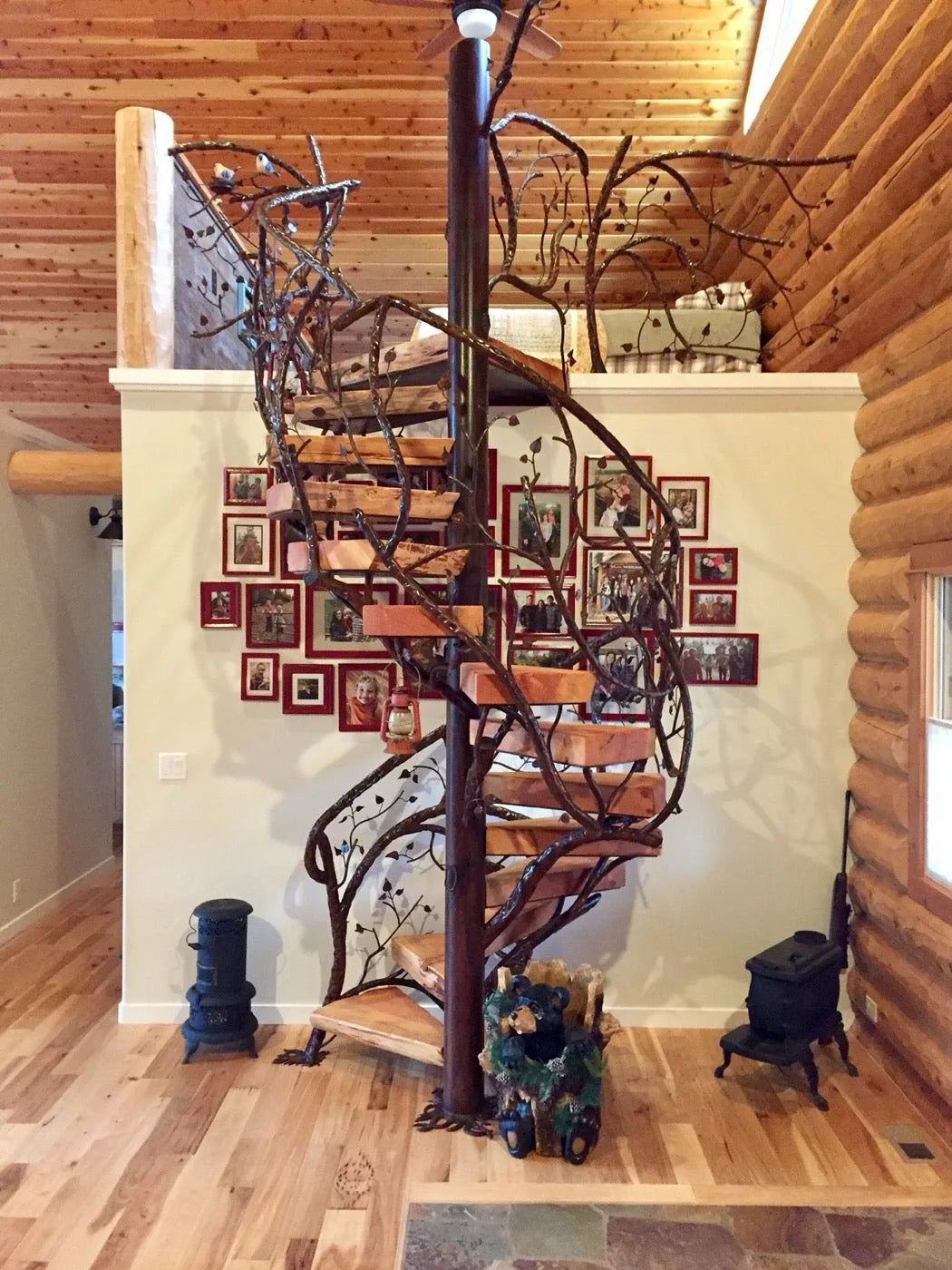 Wrought-iron spiral staircase with a tree-branch motif beside a family photo wall
