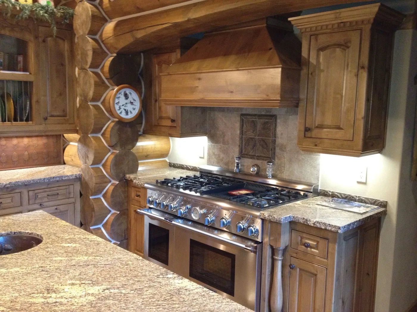 Log home kitchen with a copper-tile backsplash, birds clock, and stainless range