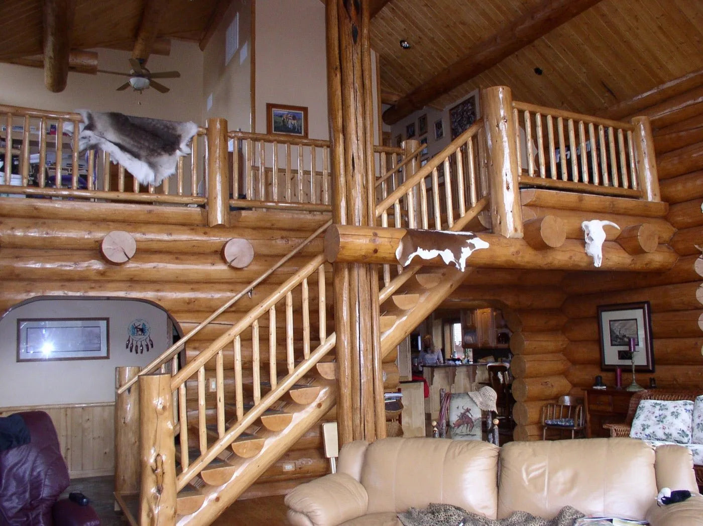 Log home great room with dual log staircases leading to a loft with animal hide accents